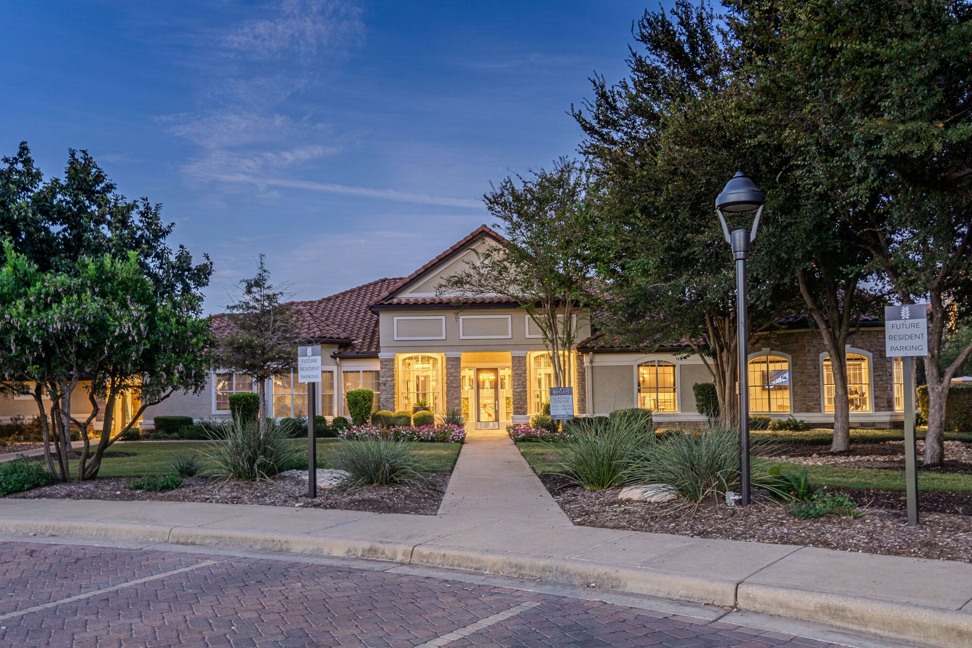 Apartment community clubhouse in Cedar Park at twilight, warm light in every window and along the walkway